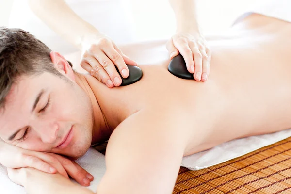 Positieve jonge man die geniet van een rug massage met hete steen — Stockfoto
