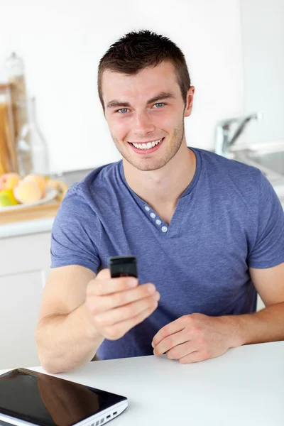 Веселый молодой человек, посылающий смс, улыбающийся в камеру — стоковое фото