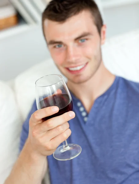 Joven carismático sosteniendo una copa de vino sentado en un sofá — Foto de Stock