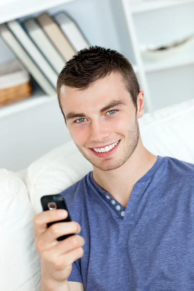 Uroczy młody człowiek wysyła tekst, uśmiechając się do kamery — Zdjęcie stockowe