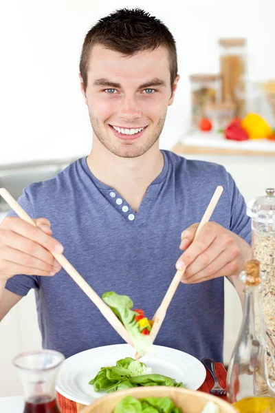 Pohledný mladý muž jíst salát se usmívá na kameru — Stock fotografie