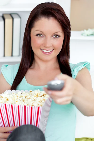 Schattig Kaukasische vrouw met een afstandsbediening en popcorn kijken naar de — Stockfoto