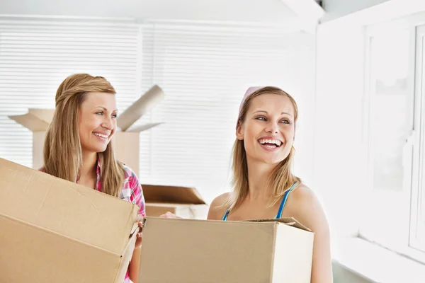 Riendo amigas sosteniendo cajas después de mudarse — Foto de Stock