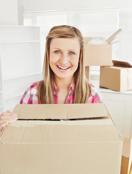 Mulher positiva segurando uma caixa de pé em sua nova casa olhando um — Fotografia de Stock