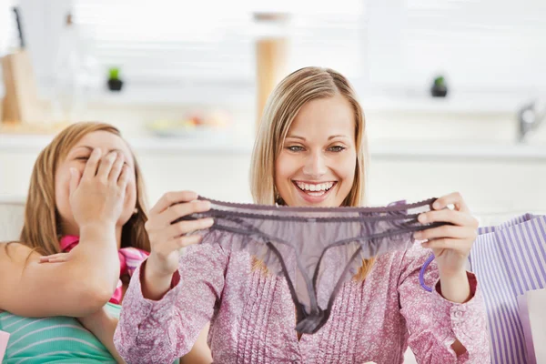 Mujeres riendo sosteniendo lencería sentadas en el sofá —  Fotos de Stock