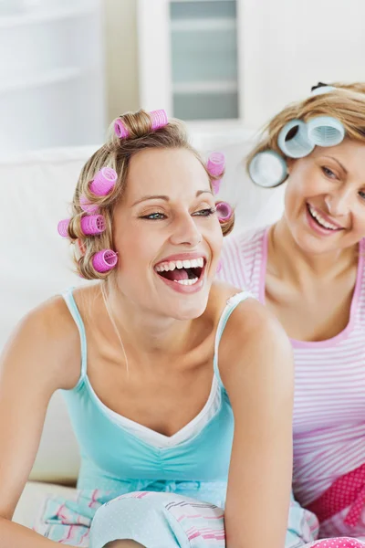 Donne che ridono indossando rulli per capelli seduti sul divano — Foto Stock