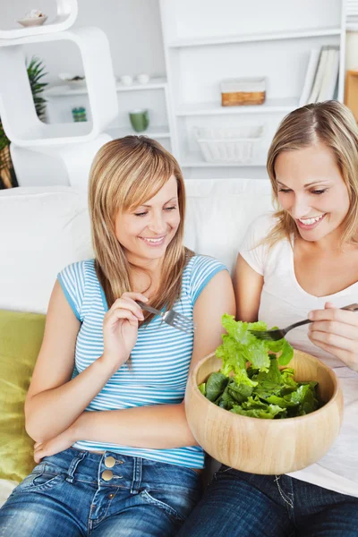 Mujeres amigas positivas comiendo una ensalada en el sofá —  Fotos de Stock