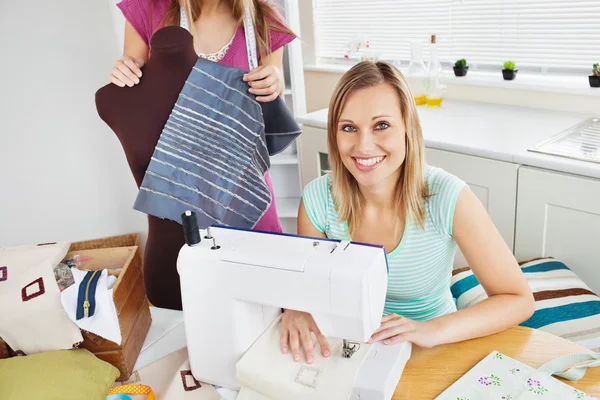 Smiling woman sewing in the kitchen with her friend — Stock Photo, Image