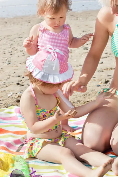 Lief klein meisje met behulp van zonnebrandcrème op het strand — Stockfoto