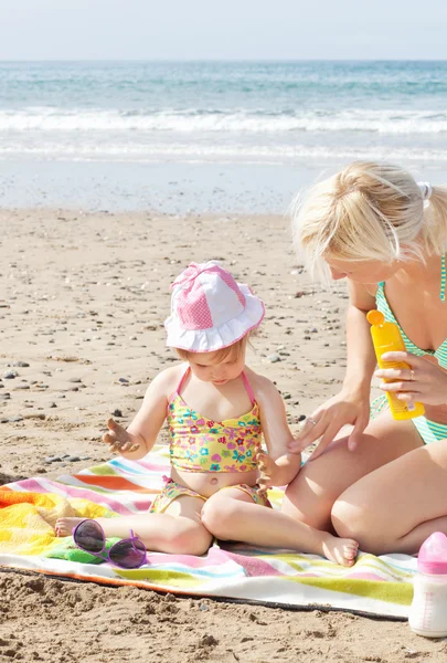 Liten flicka med solkräm på stranden — Stockfoto