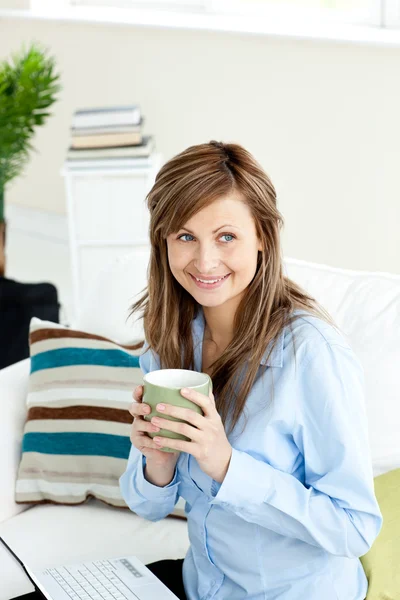 Привлекательная деловая женщина пьет кофе, сидя на ноутбуке — стоковое фото