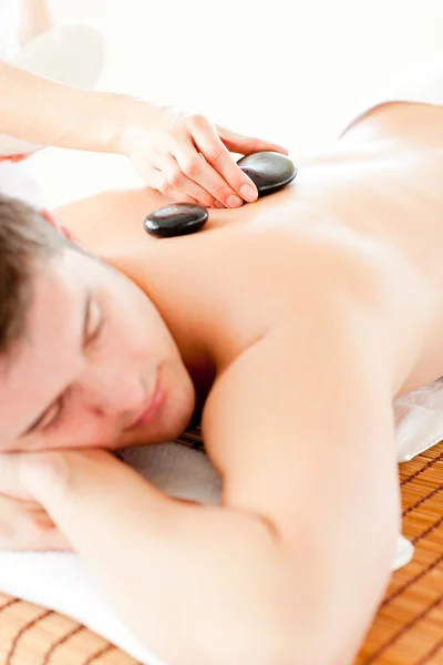 Расслабленный молодой человек получает массаж спины горячим камнем — стоковое фото
