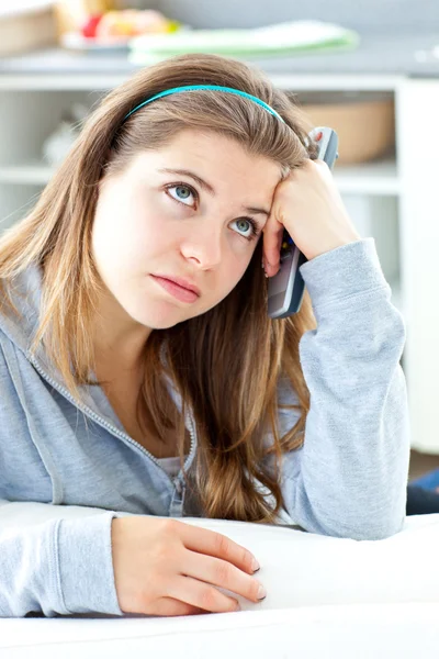 Bored young woman holdinga remote sitting in the kitchen — Stock Photo, Image