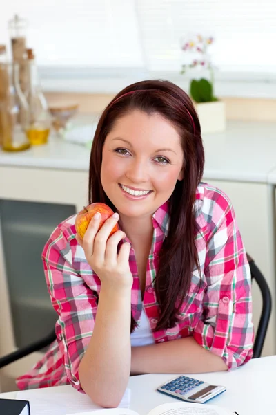 Mulher caucasiana encantada segurando uma maçã sentada na cozinha — Fotografia de Stock