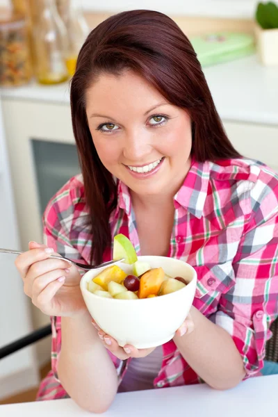 Mulher brilhante comendo uma salada de frutas no café da manhã na cozinha — Fotografia de Stock