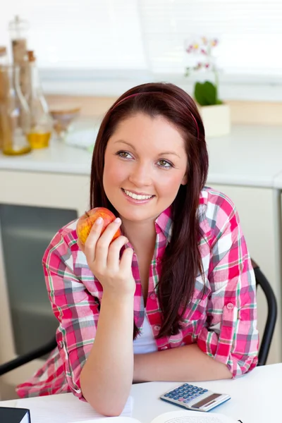 Radiante mujer caucásica sosteniendo una manzana sentada en la cocina — Foto de Stock