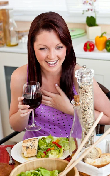 Mulher encantada comendo sua refeição segurando um copo de vinho em casa — Fotografia de Stock