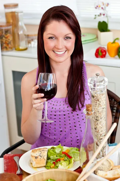 Charming woman eating her meal holding a glass of wine at home — Stock Photo, Image