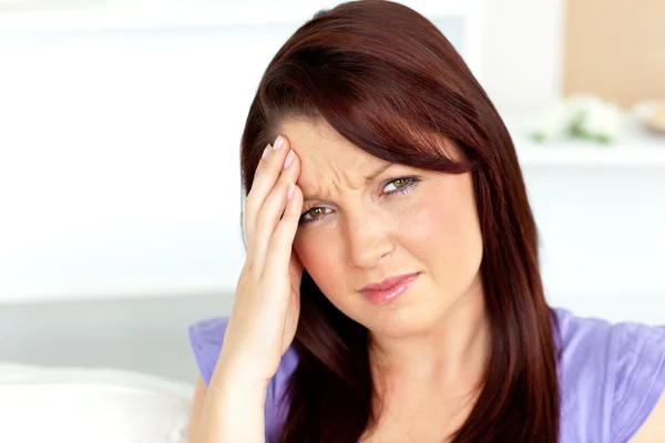 Cute woman with a headache sitting on a sofa at home — Stock Photo, Image