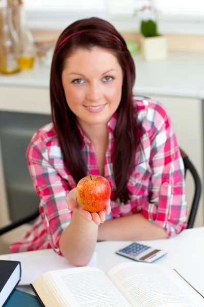 Mujer caucásica seria sosteniendo una manzana sentada en la cocina — Foto de Stock