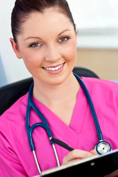 Serious female surgeon with a stethoscope writing in a clipboard — Stock Photo, Image