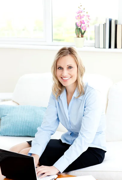 Усміхнена бізнес-леді використовує свій ноутбук, сидячи на дивані — стокове фото