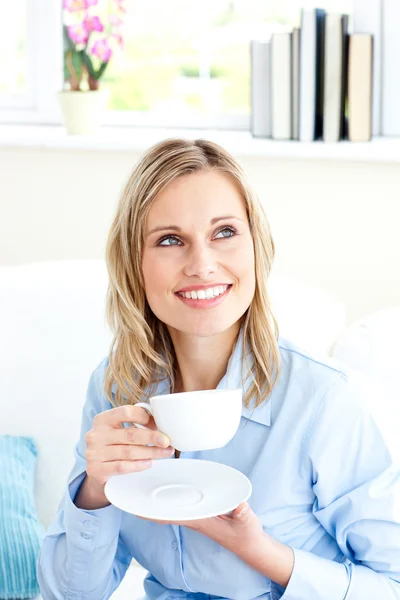 Captivating businesswoman holding a cup sitting on a sofa — Stock Photo, Image