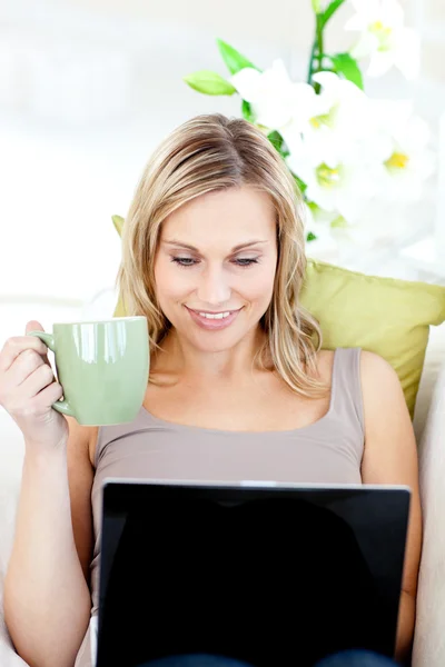 Donna caucasica seduta davanti al suo computer portatile e con in mano una tazza — Foto Stock
