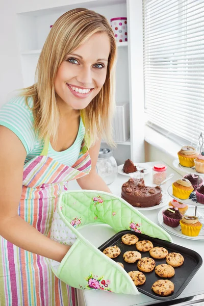 Mulher sorridente segurando biscoitos na cozinha — Fotografia de Stock