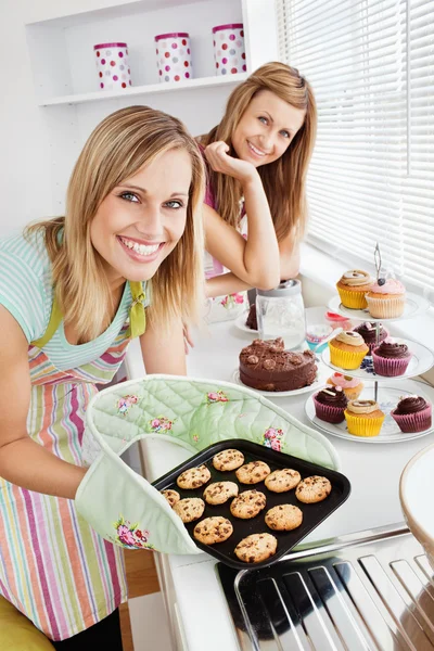 Felices amigas sosteniendo galletas en la cocina — Foto de Stock