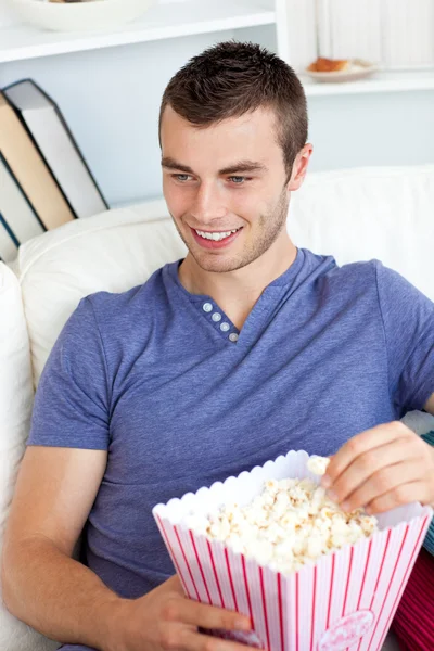 Beyaz adam yeme patlamış mısır kanepede gülüyor — Stok fotoğraf