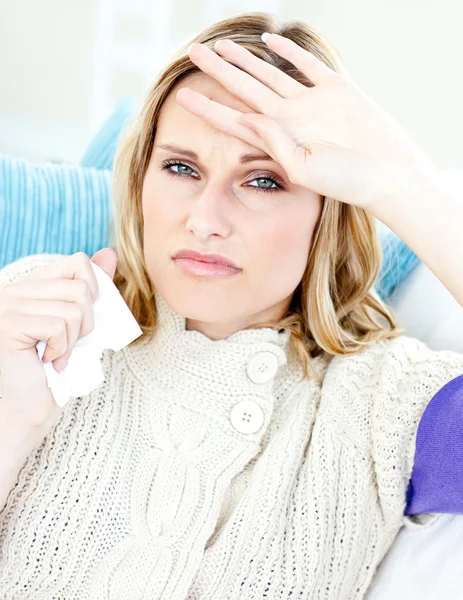 Dejected woman lying on a sofa with tissues and feeling her temp — Stock Photo, Image