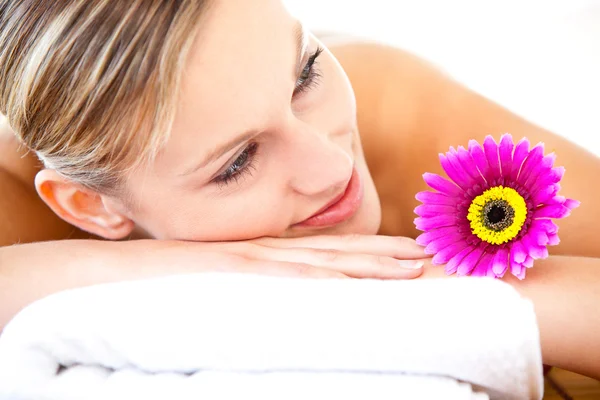 Close-up de uma mulher brilhante deitada em uma mesa de massagem com um flowe — Fotografia de Stock