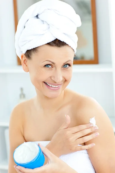 Uroczy młoda kobieta z ręcznikiem wprowadzenie krem na twarz w t — Zdjęcie stockowe
