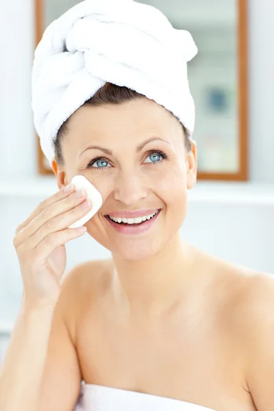 Sorrindo jovem mulher com uma toalha colocando creme em seu rosto em th — Fotografia de Stock