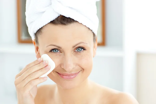 Giovane donna gioiosa con un asciugamano mettendo crema sul viso nel — Foto Stock