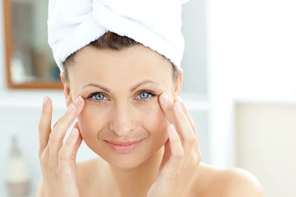 Carino giovane donna con un asciugamano mettendo crema sul suo viso nel b — Foto Stock