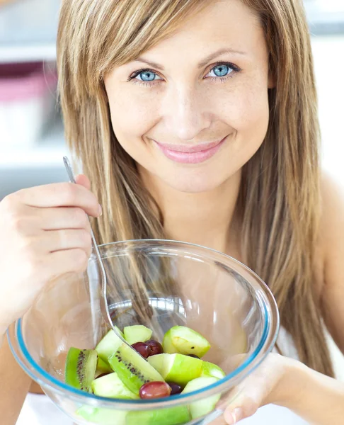 Wesoły kobieta jedzenie sałatki owocowej, uśmiechając się do kamery w ki — Zdjęcie stockowe