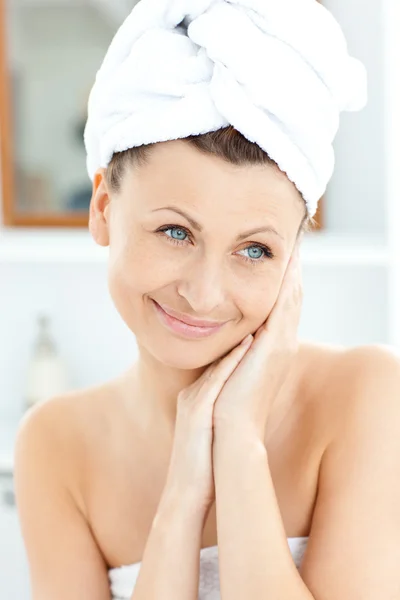 Mujer joven radiante con una toalla poniendo crema en su cara en th — Foto de Stock