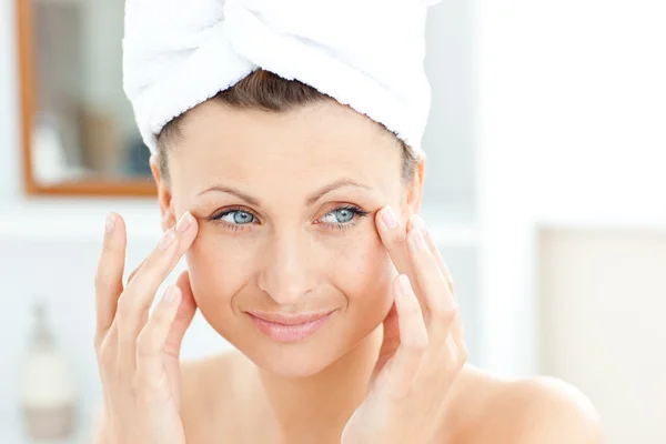 Attraente giovane donna con un asciugamano mettendo crema sul viso in — Foto Stock