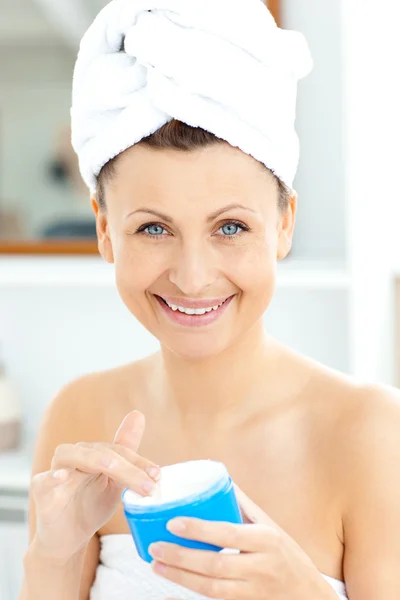 Roztomilá mladá žena s ručníkem dát krém na tvář v b — Stock fotografie