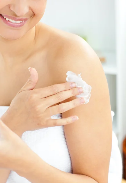 Happy young woman with a towel putting cream on her face in the — Stock Photo, Image