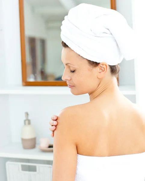 Blij jonge vrouw met een handdoek invoering crème op haar gezicht in th — Stockfoto