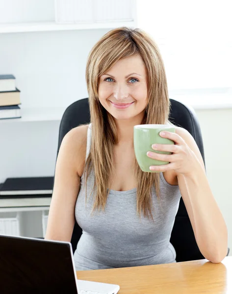 Glödande affärskvinna innehar en kopp kaffe med sin laptop en — Stockfoto