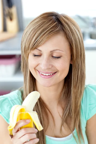 Smiling young woman holding a banana in the kitchen — Stock Photo, Image