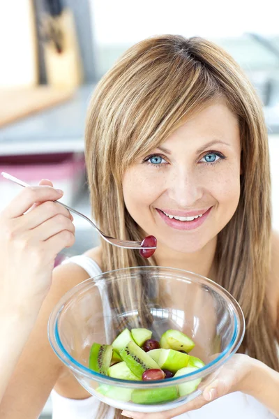 Προσωπογραφία γυναίκας ακτινοβόλο τρώει μια σαλάτα φρούτων στην κουζίνα — Φωτογραφία Αρχείου