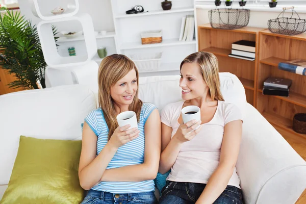 Två söta kvinnor dricka kaffe tillsammans på en soffa — Stockfoto