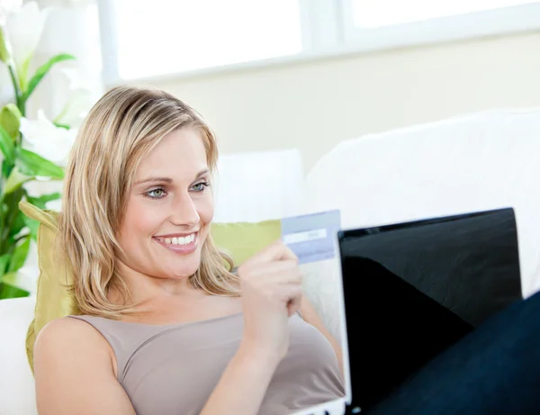 Hermosa mujer acostada en un sofá con un portátil con una tarjeta —  Fotos de Stock