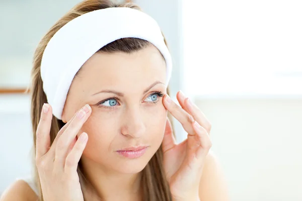 Mujer joven poniendo crema en su cara con una diadema en la — Foto de Stock