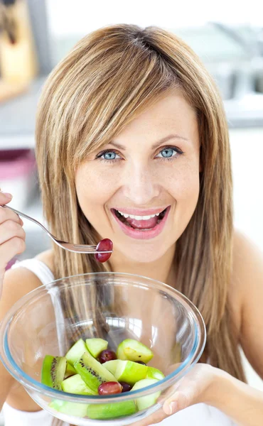 Mujer alegre comiendo una ensalada de frutas sonriendo a la cámara en el ki —  Fotos de Stock